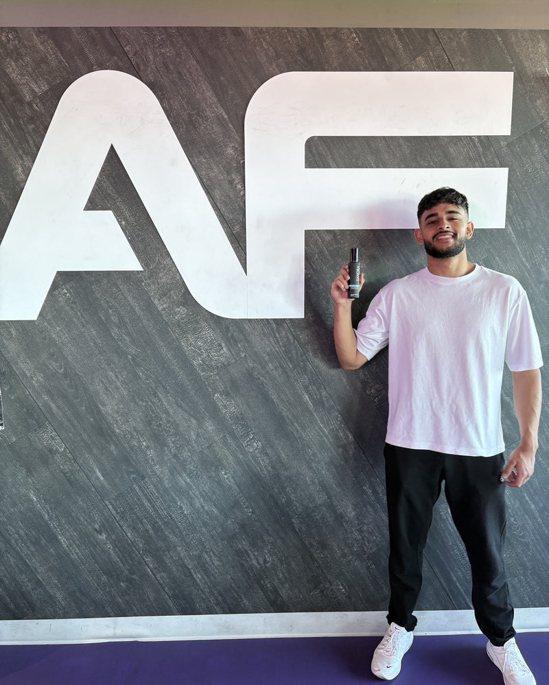 Harman, founder of SANORA, holding a bottle in front of the Anytime Fitness logo