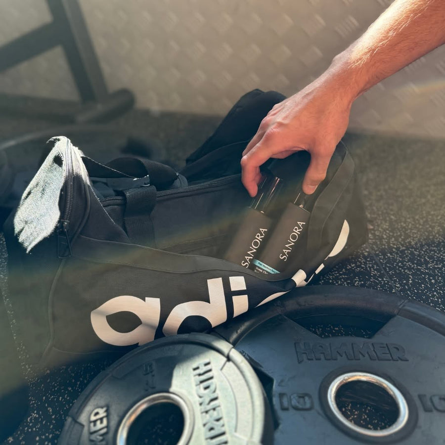 Two SANORA bottles in a gym bag beside weight plates